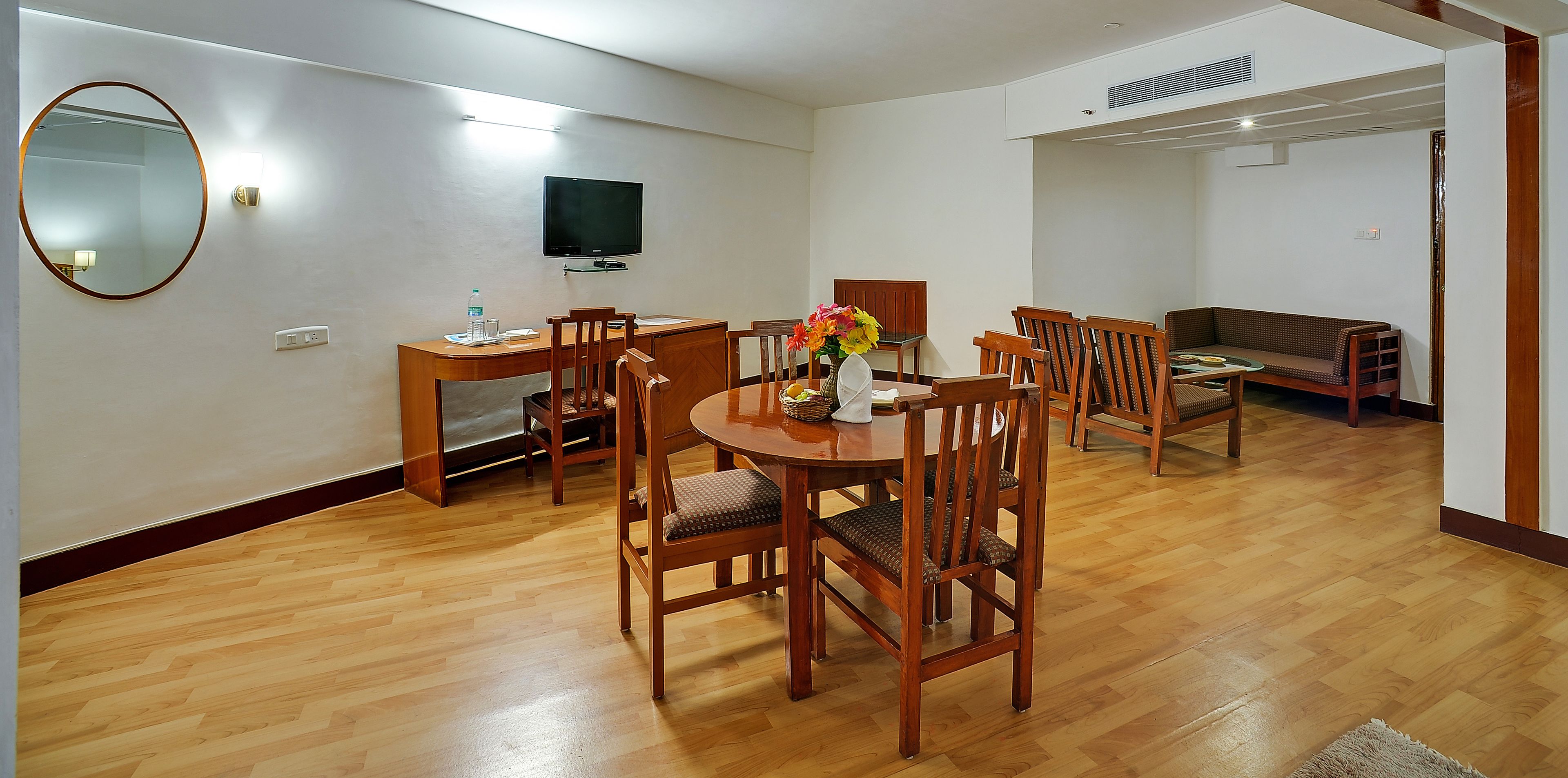 Un coin repas avec une table et des chaises en bois, un téléviseur fixé au mur et un canapé à l’arrière-plan.