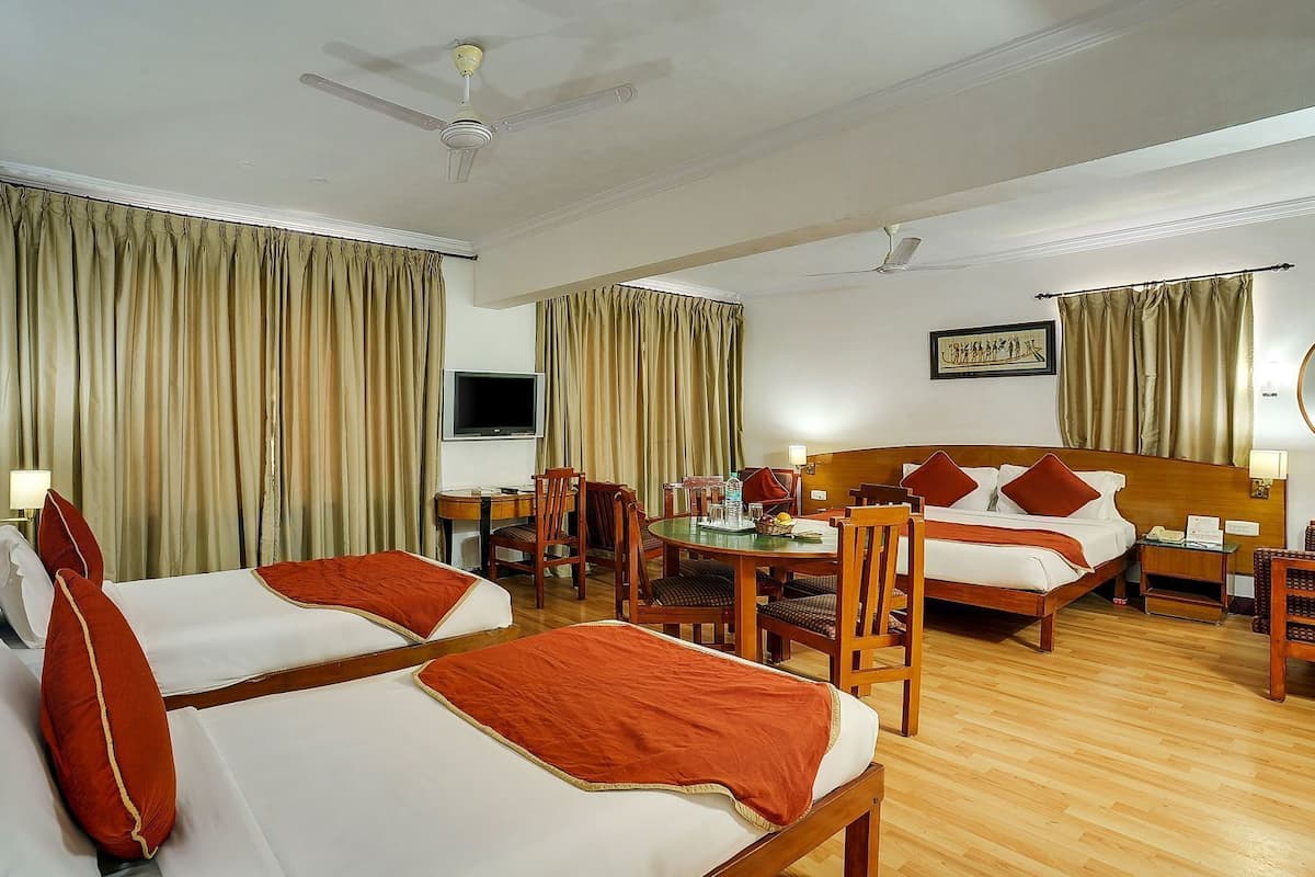 A hotel room with two beds, a dining table, chairs, a TV, and a ceiling fan.