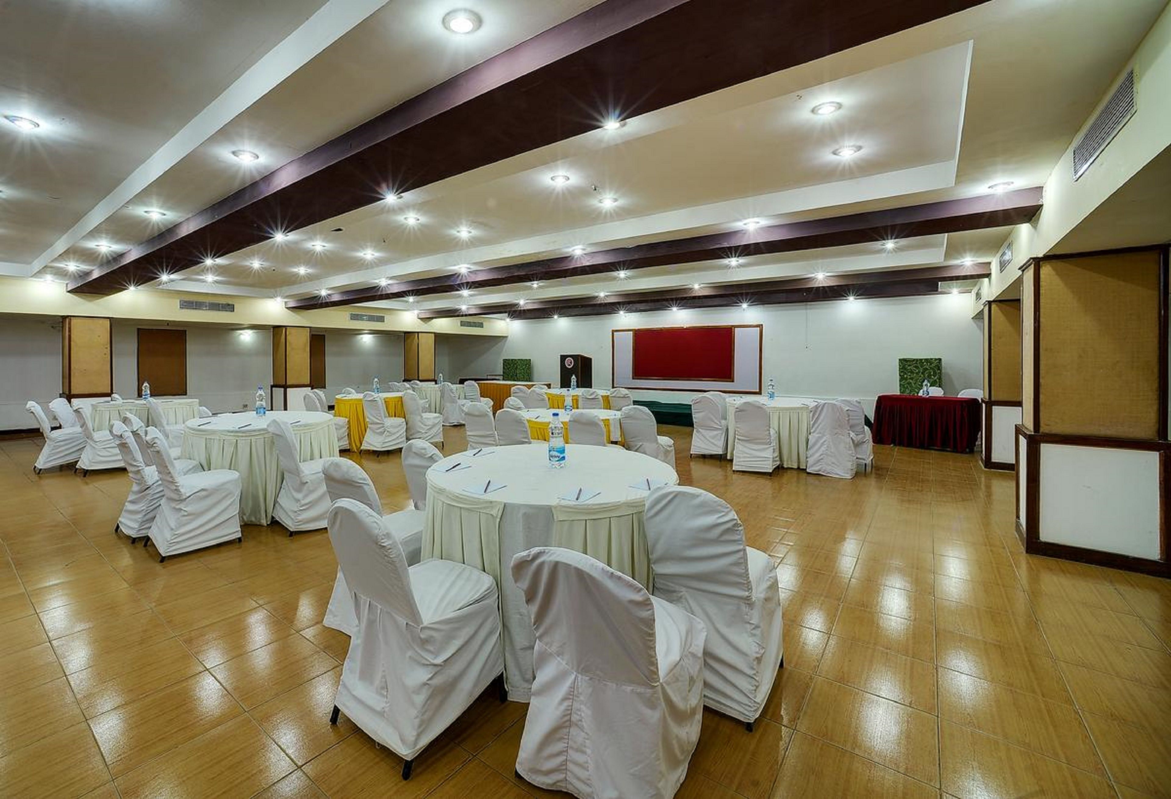 A conference room with round tables, white chairs, and a red screen.