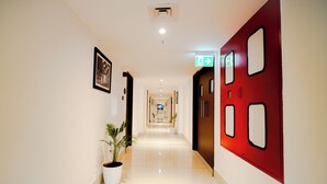 A hotel corridor with a polished floor, framed artwork on the walls, and potted plants.