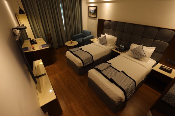 A hotel room with two beds, a desk, a chair, a small table, and a window with curtains.