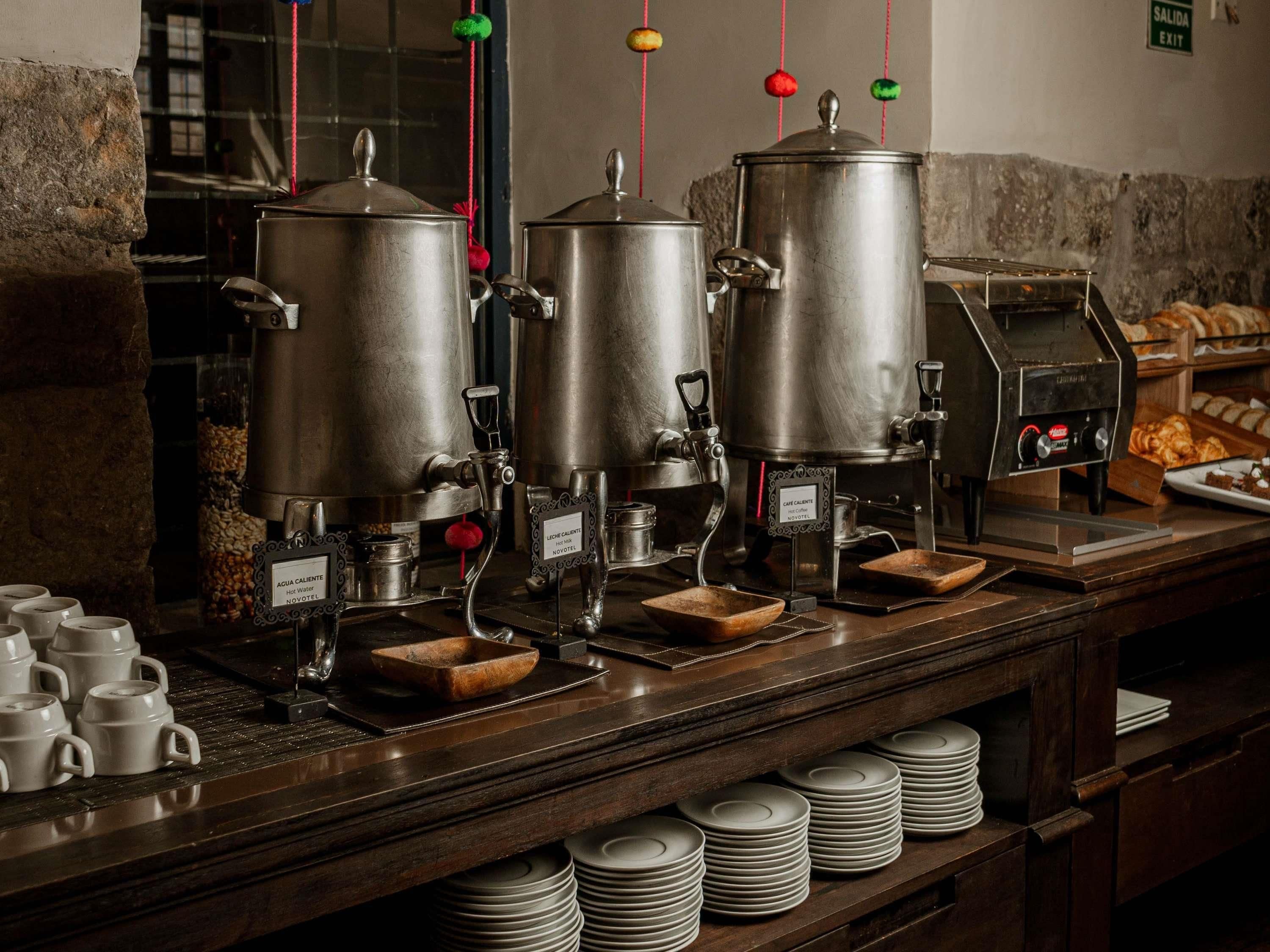 Montaje de bufé con dispensadores de agua caliente, una máquina de café y una selección de productos horneados.