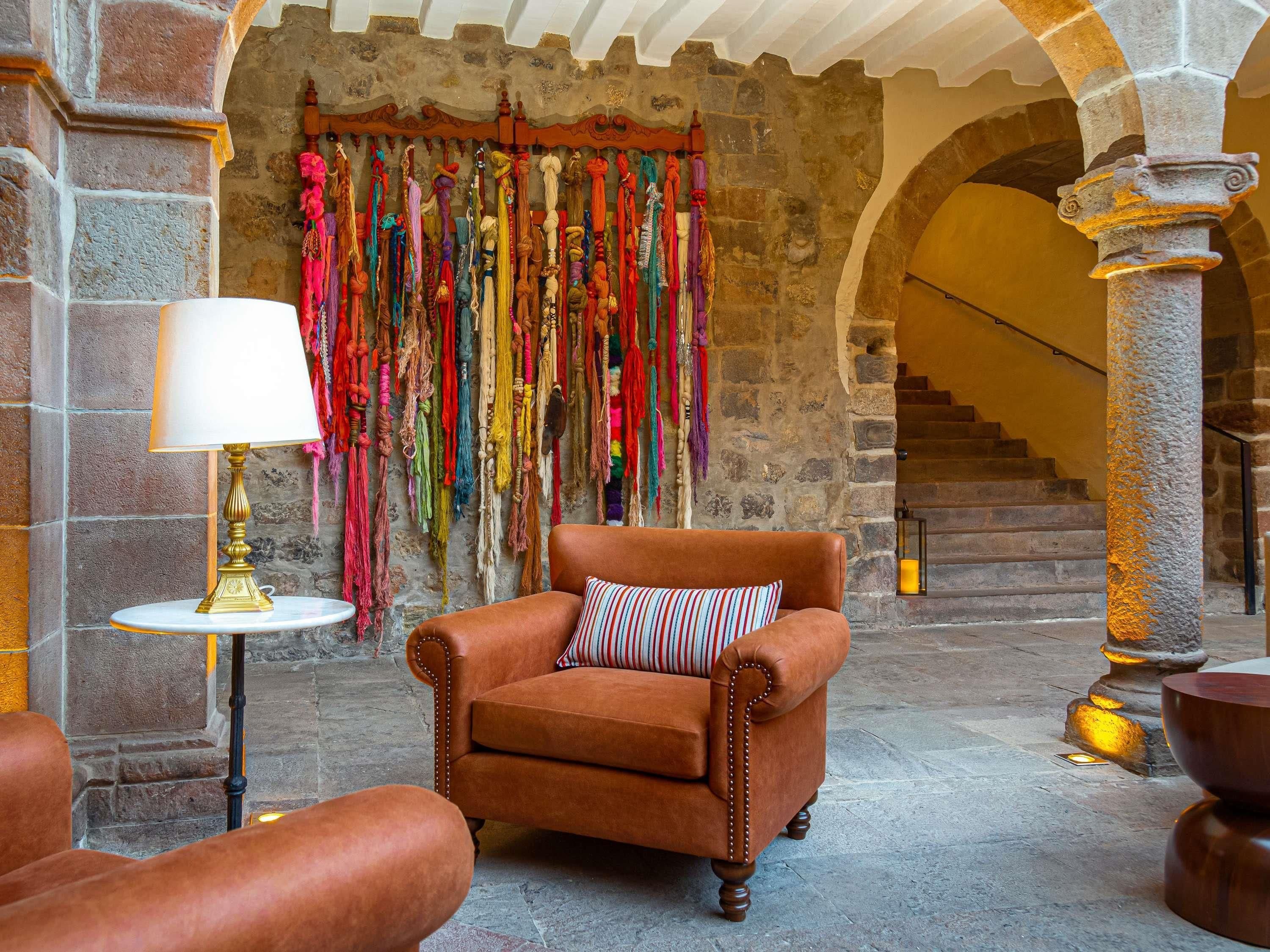 A stone-walled room with a leather armchair, a small table with a lamp, and a colorful tapestry on the wall.