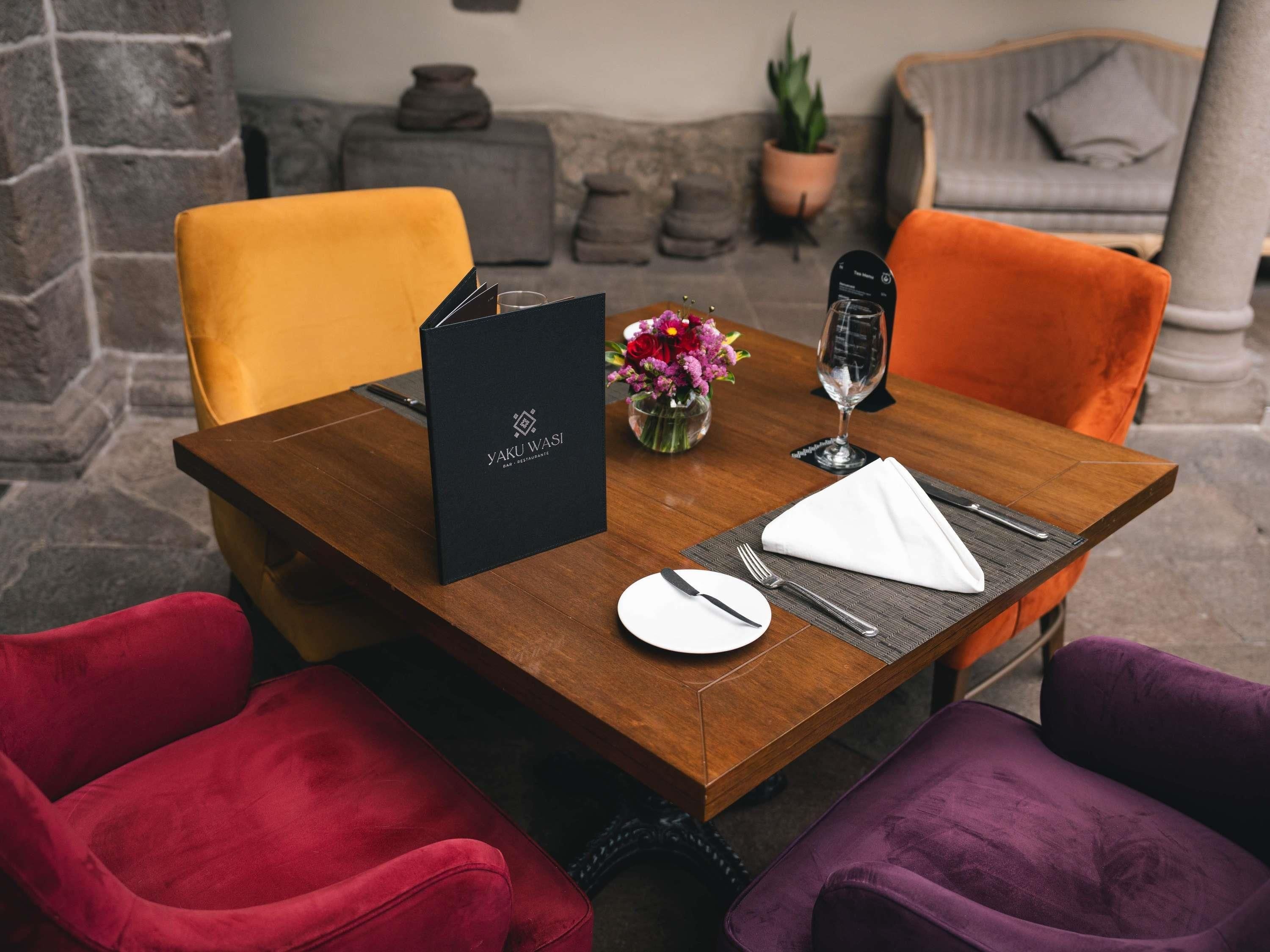 A dining table set with a black menu, a glass of water, a white plate, and cutlery.