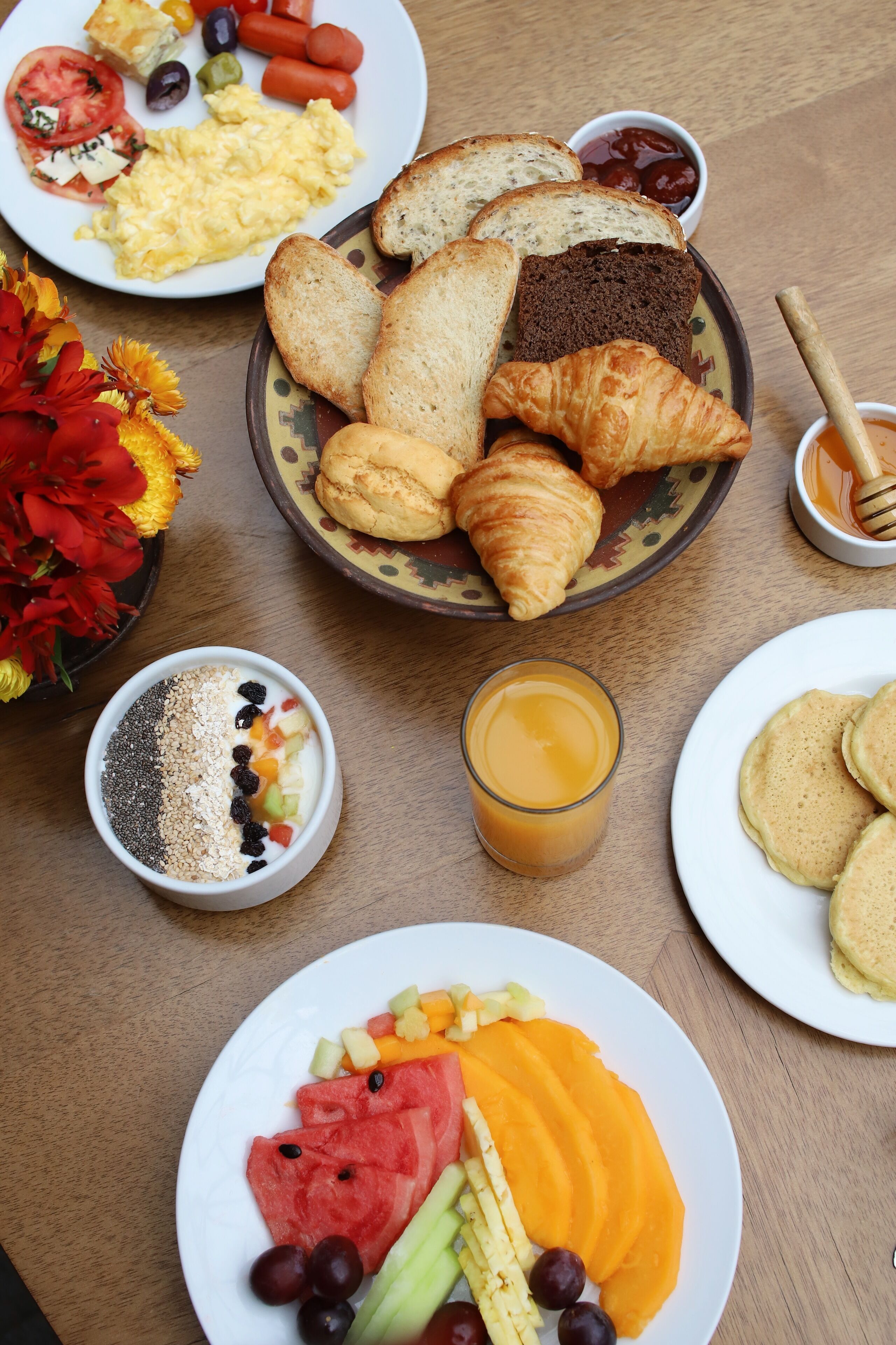 Una mesa de desayuno con diversos alimentos como tostadas, cruasanes, huevos revueltos y fruta.