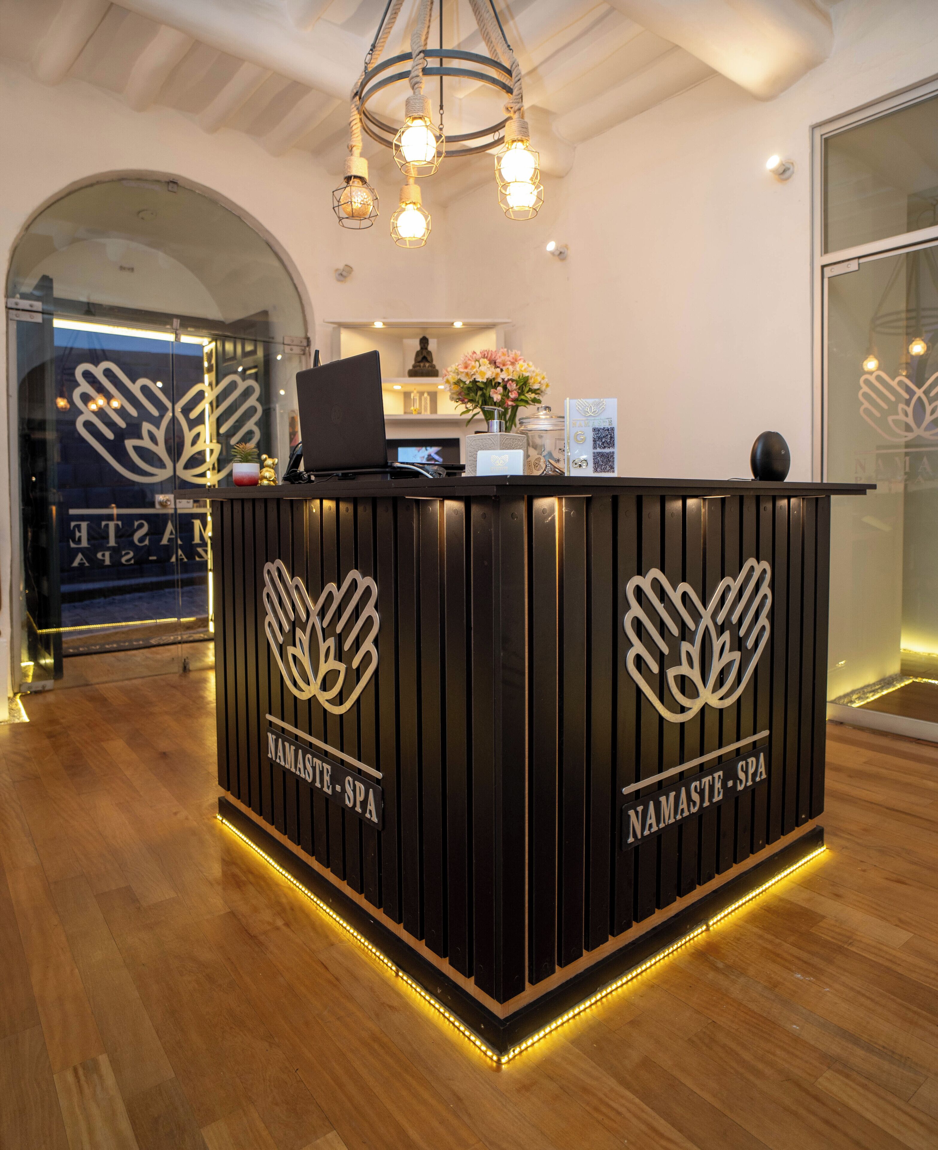 A reception desk with 'Namaste Spa' branding, a laptop, and a vase with flowers.