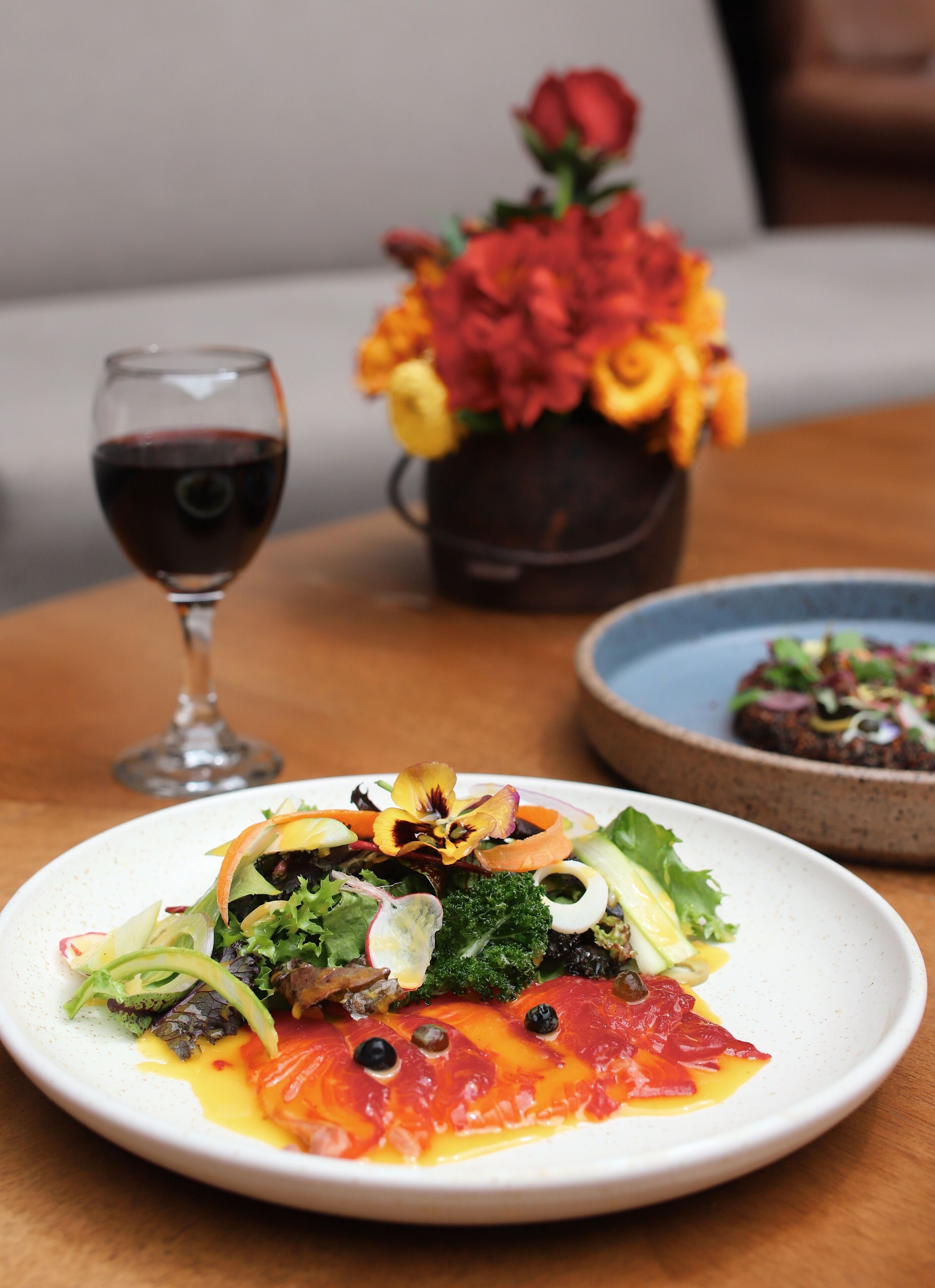 A dining table with a plate of food, a glass of red wine, and a vase of flowers.