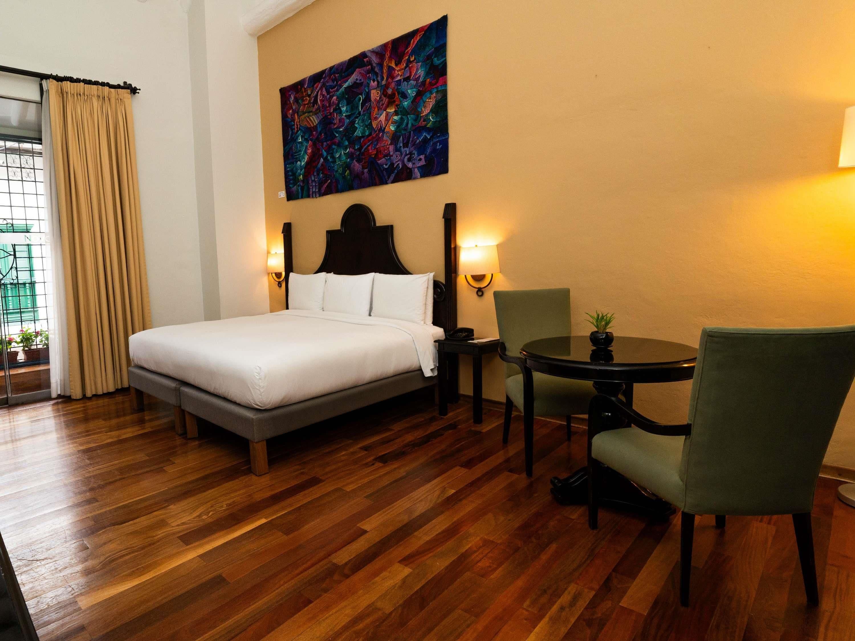 Ein Hotelzimmer mit Bett, Sessel, Tisch und einem Bild an der Wand.