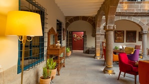 Un corredor espacioso con arcos de piedra, una puerta roja y un área de descanso con sillas coloridas.