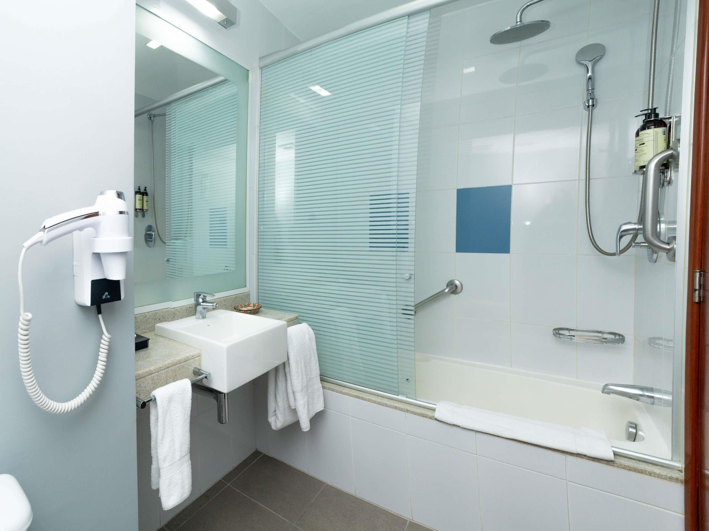 Un baño moderno con cabina de ducha de vidrio, un lavamanos blanco y un secador de pelo montado en la pared.