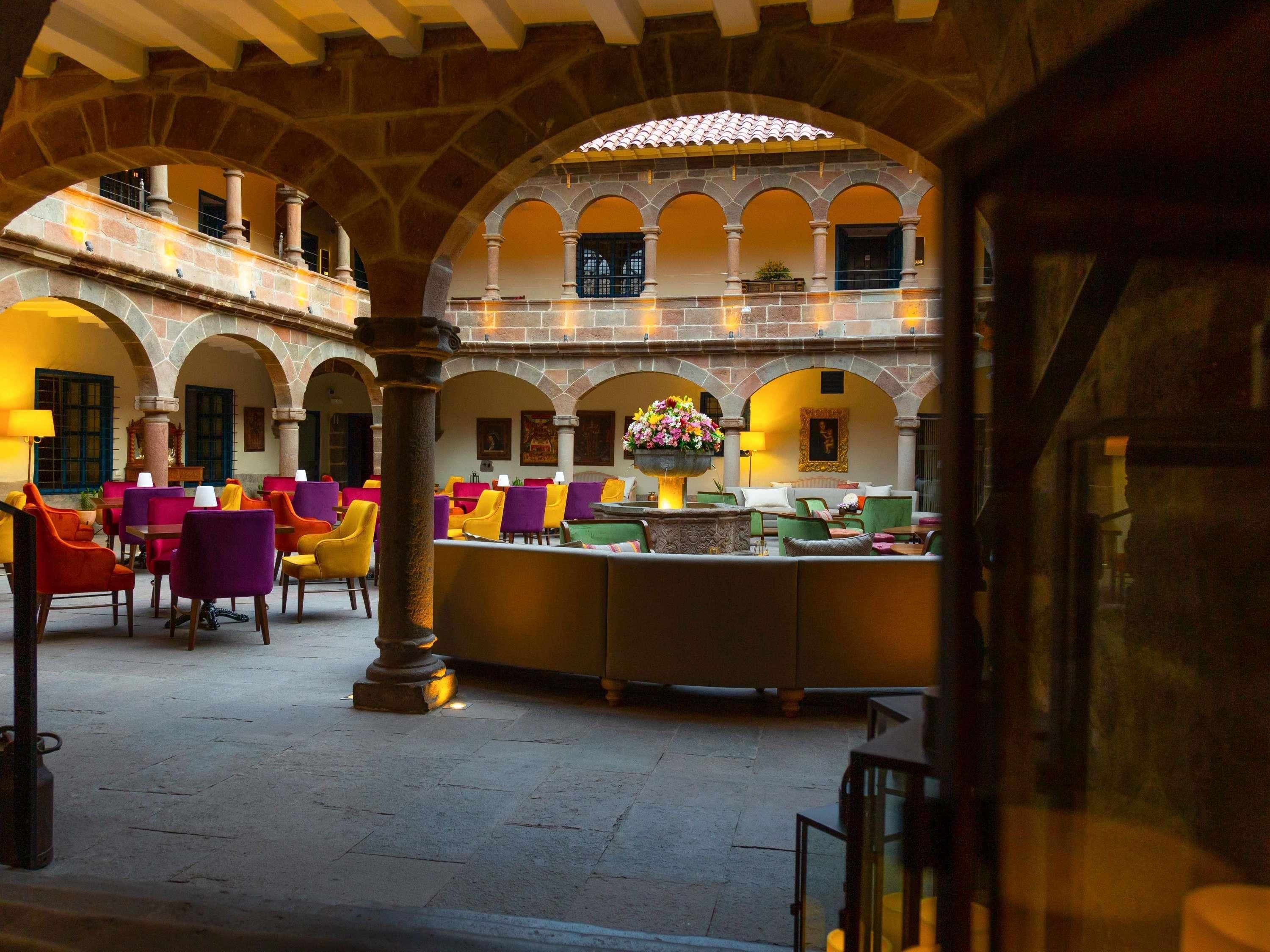 Un patio con varias zonas de estar, arcos de piedra y una fuente central.