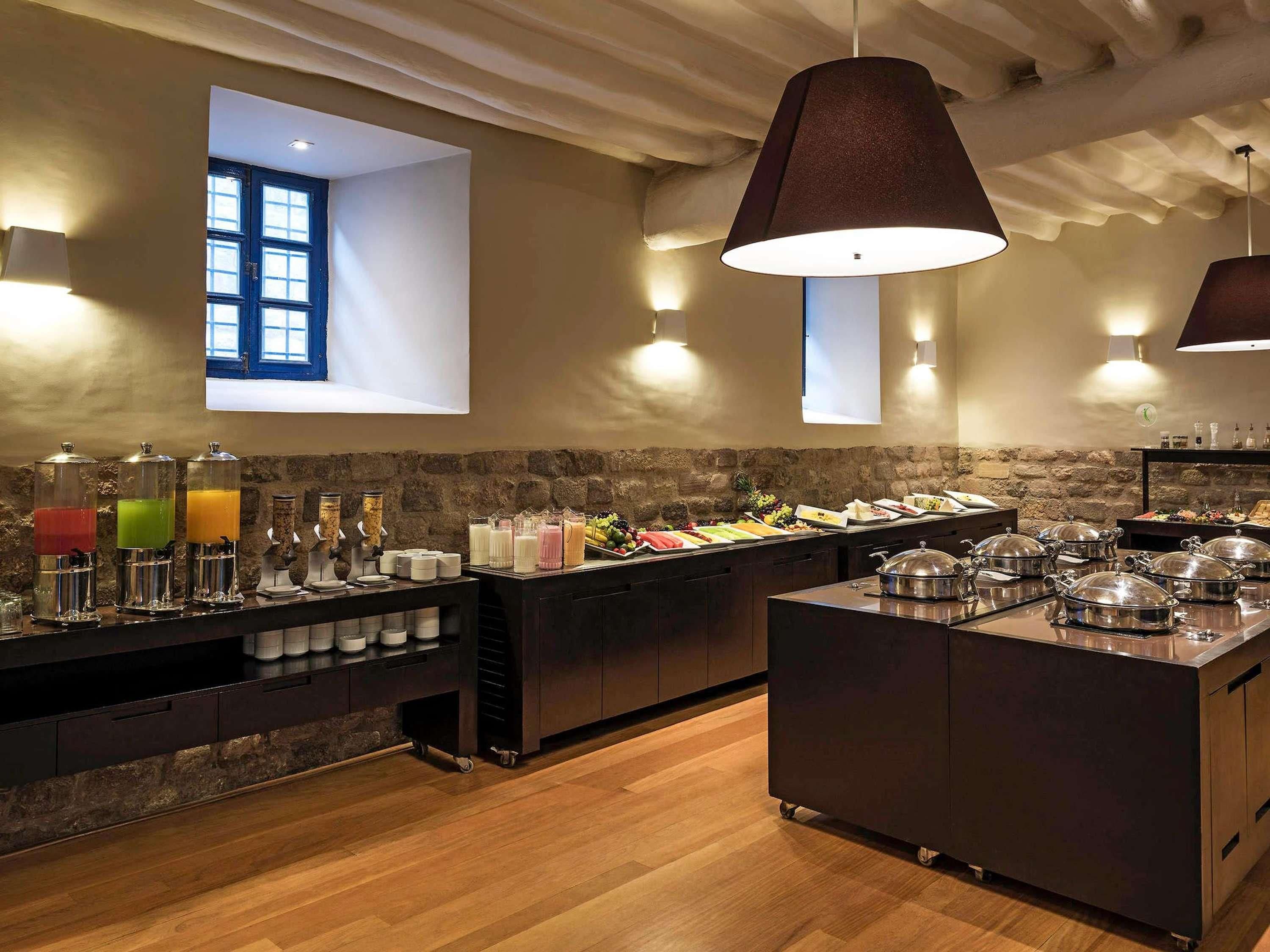 A buffet setup with various food items and beverages, a stone wall, and a window with natural light.