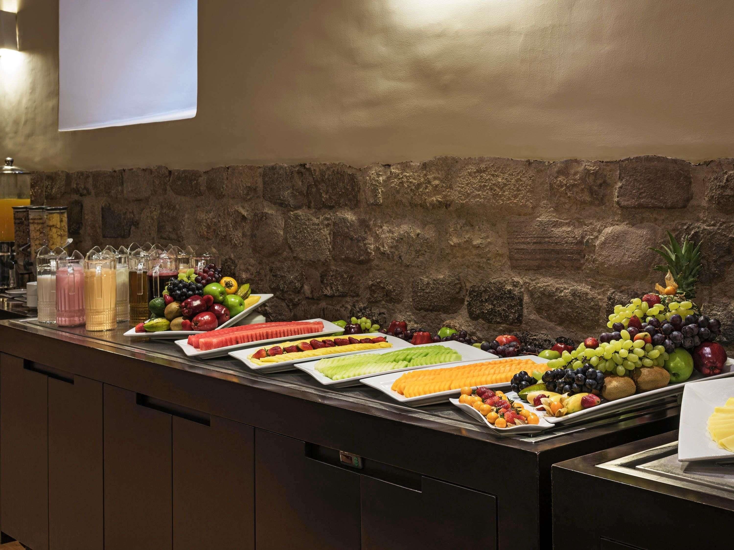 Een buffet met een achtergrond van een stenen muur, diverse soorten fruit en drankjes.
