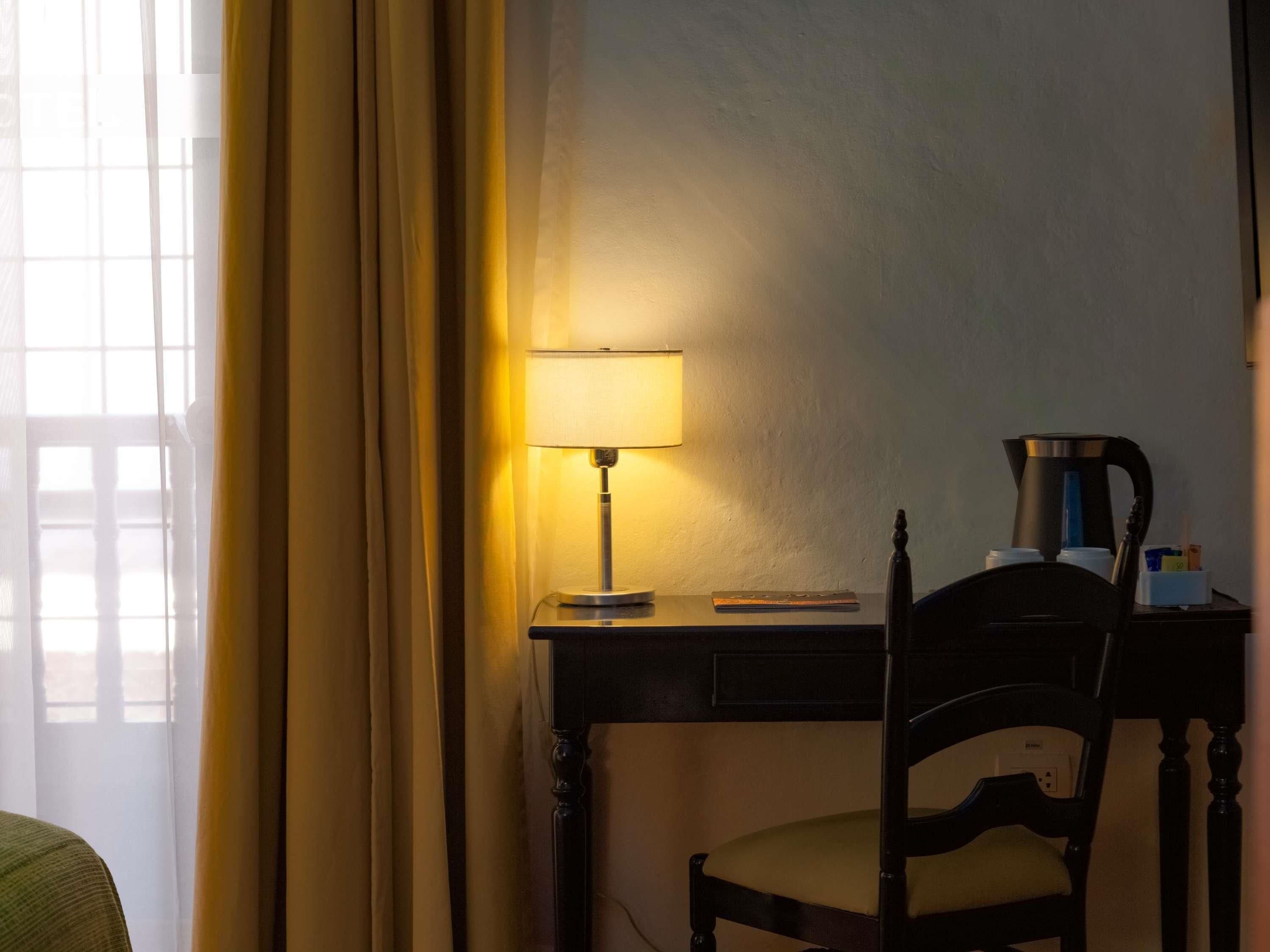 Una habitación de hotel con escritorio, silla, lámpara y cafetera.