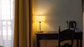 Una habitación de hotel con escritorio, silla, lámpara y cafetera.