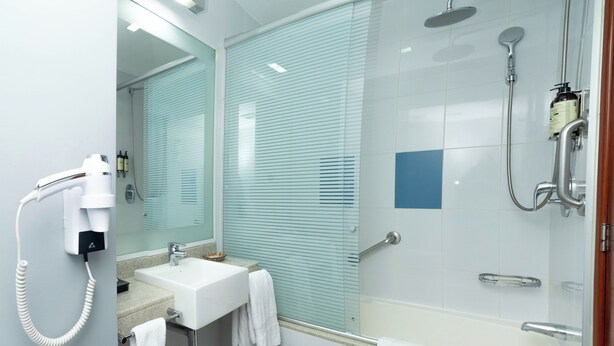 Un baño moderno con ducha de vidrio, un lavabo blanco y un secador de pelo montado en la pared.