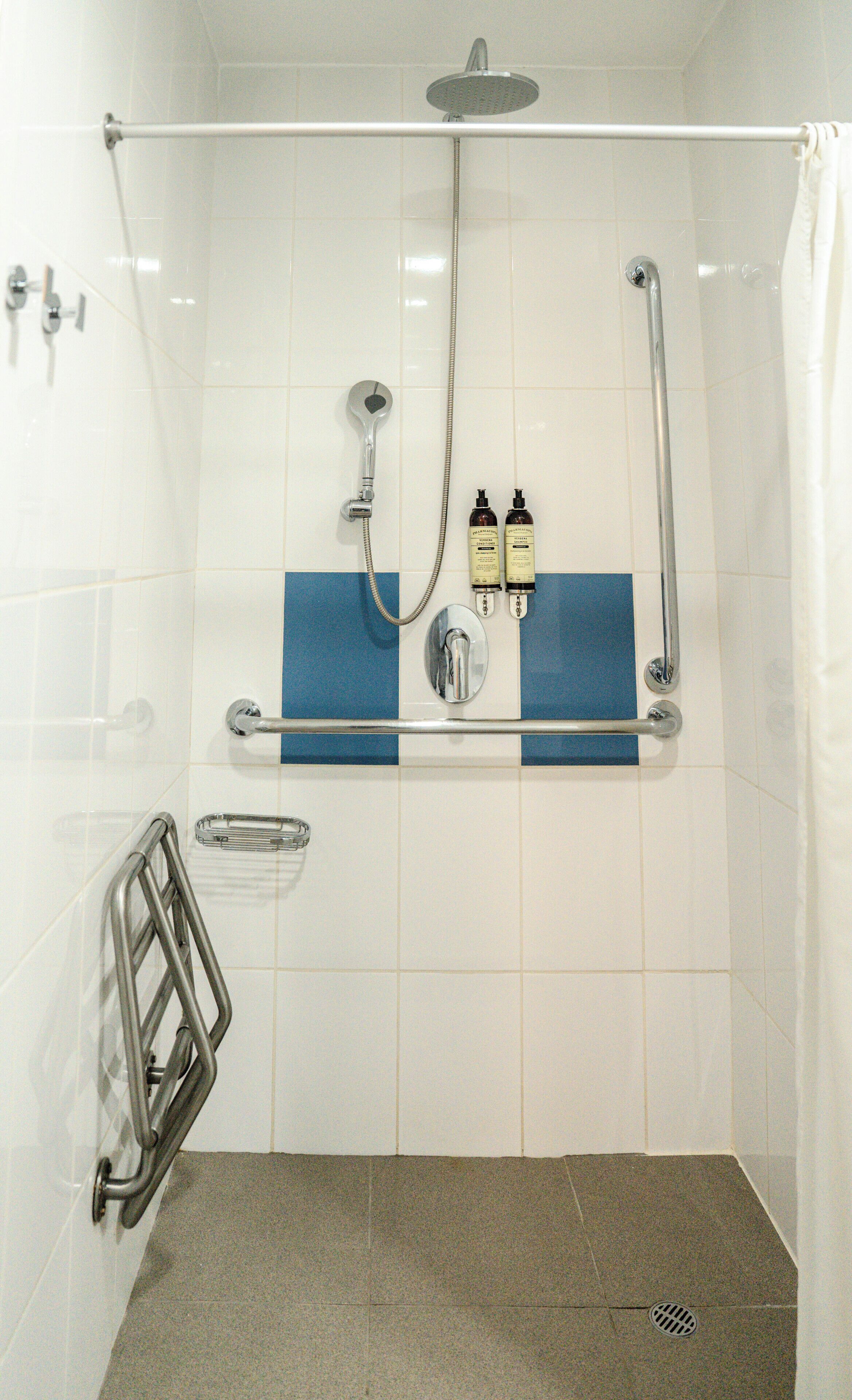 Área de chuveiro com chuveiro manual, irrigador manual e bocal de chuveiro manual. Há dois frascos de shampoo e condicionador em uma prateleira.