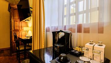 A hotel room with a dining table set for two, a coffee machine, and a window with curtains.