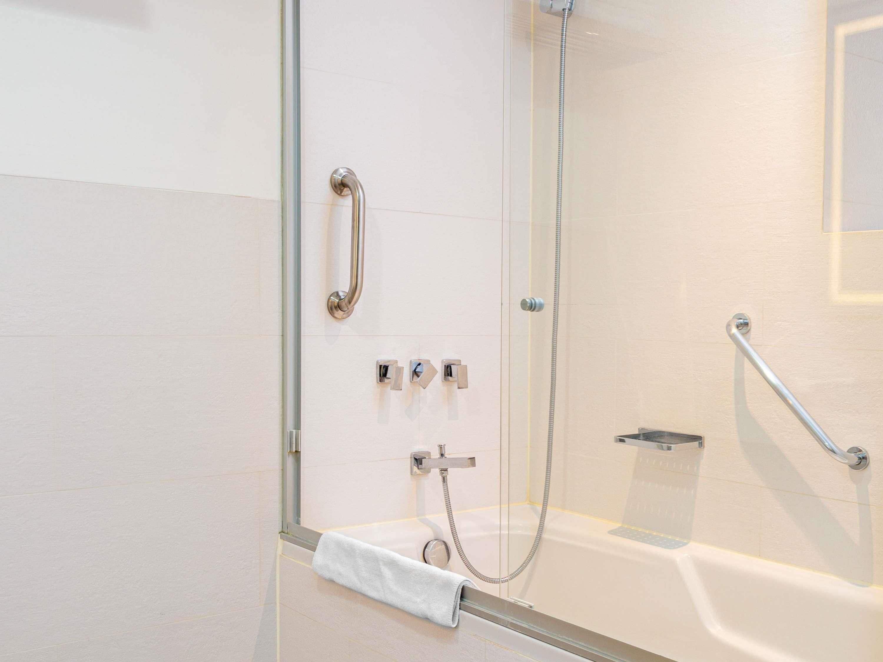 Un baño moderno con cabina de ducha de vidrio, ducha de mano, barra de apoyo y toallero.