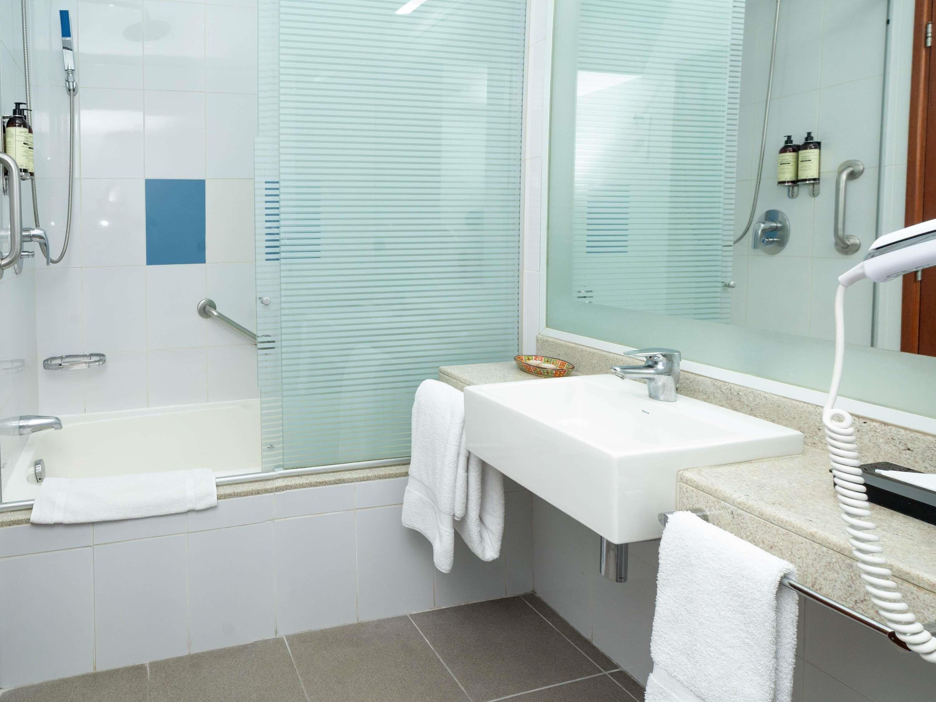 A modern bathroom with a glass shower enclosure, a white sink, and a handheld showerhead.