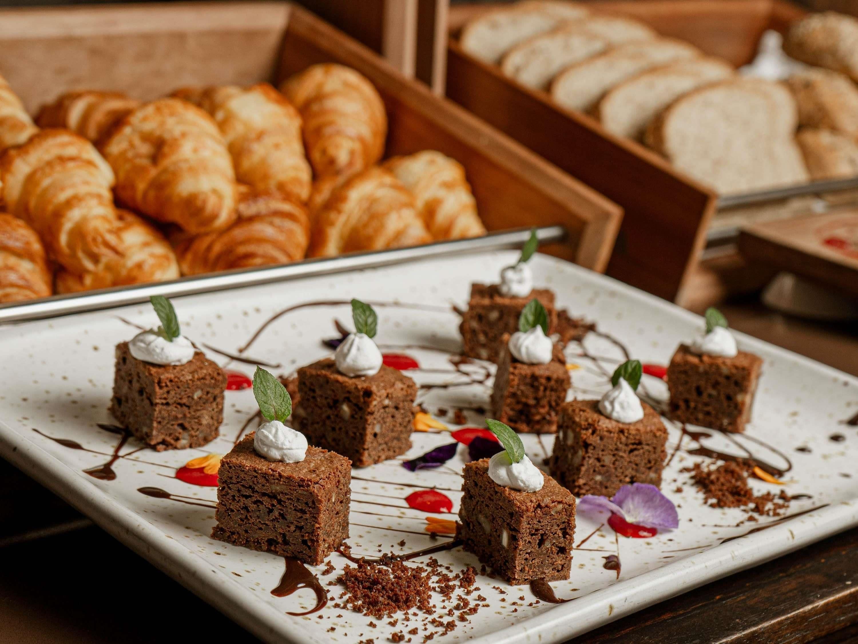 A dessert display with chocolate squares topped with whipped cream and mint leaves, surrounded by pastries.