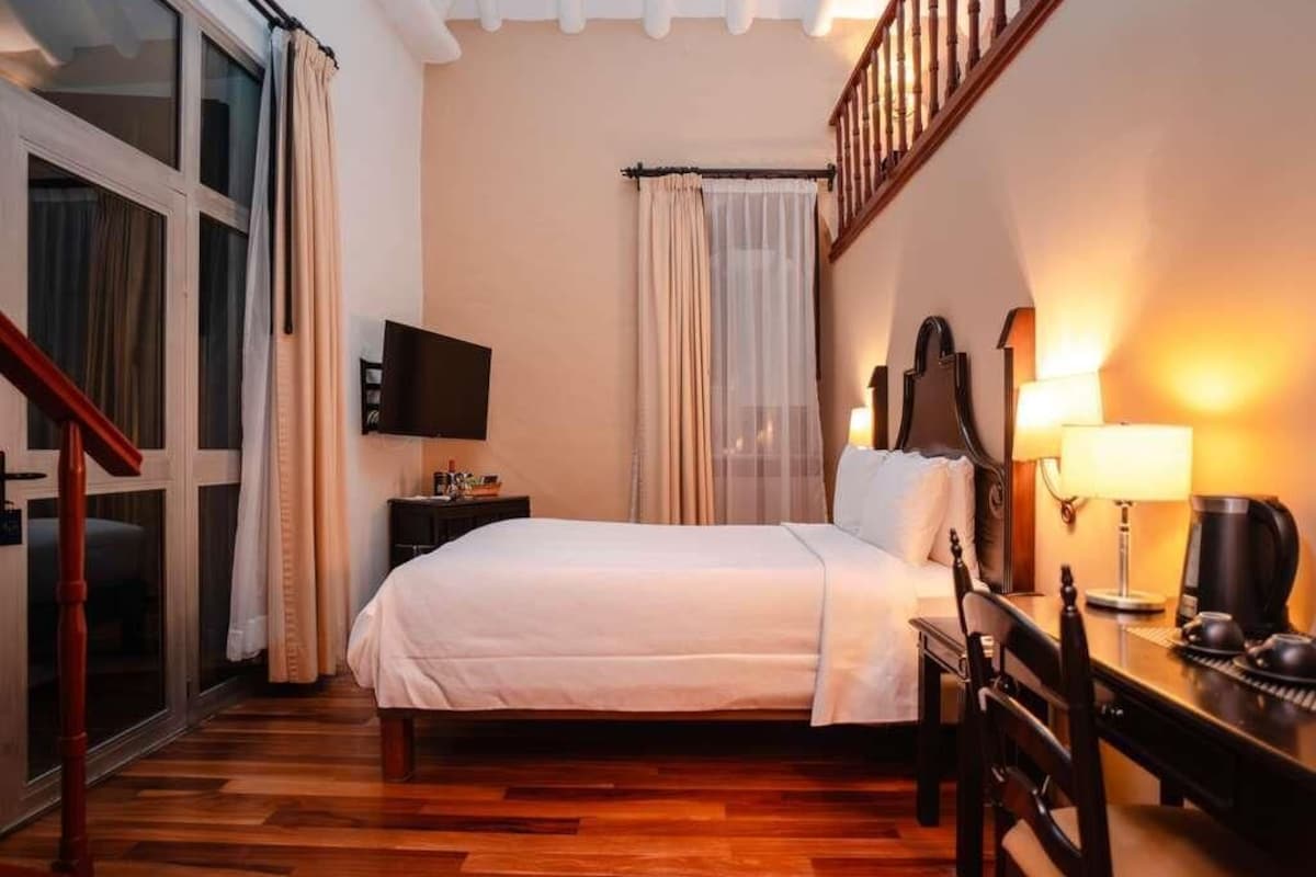 A hotel room with a bed, a desk with a lamp, a television, and a staircase.