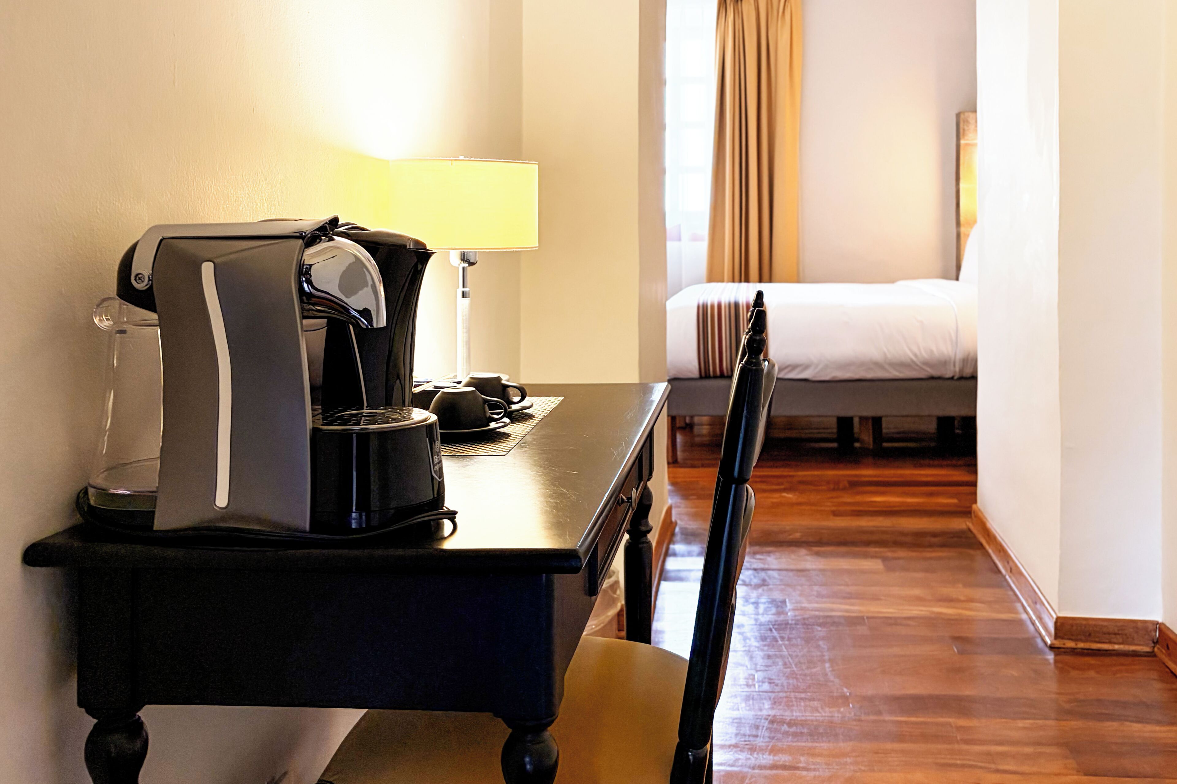 Una habitación de hotel con una cama, un escritorio con cafetera y una silla.
