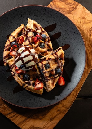 A plate of waffles with strawberries and blueberries, topped with chocolate sauce and a scoop of ice cream.