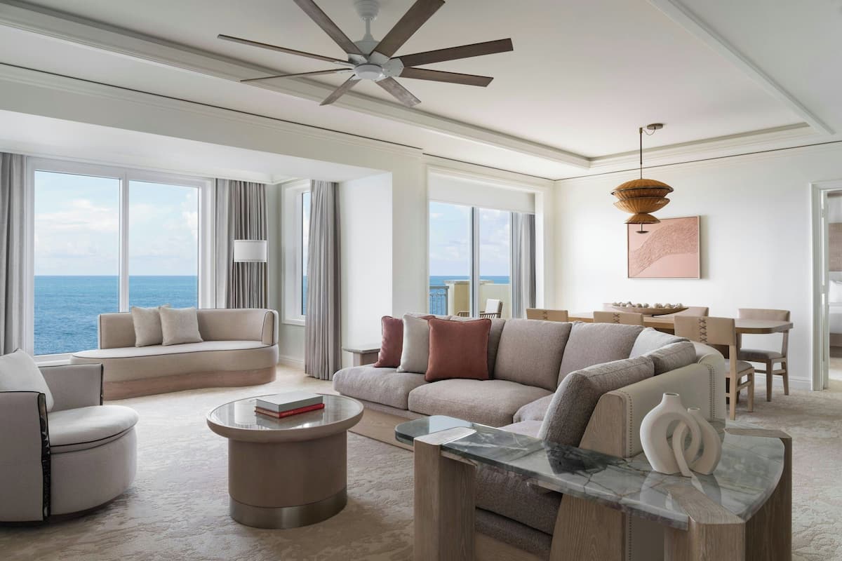 A spacious living room with a large sofa, a round coffee table, and a dining area with a view of the ocean.