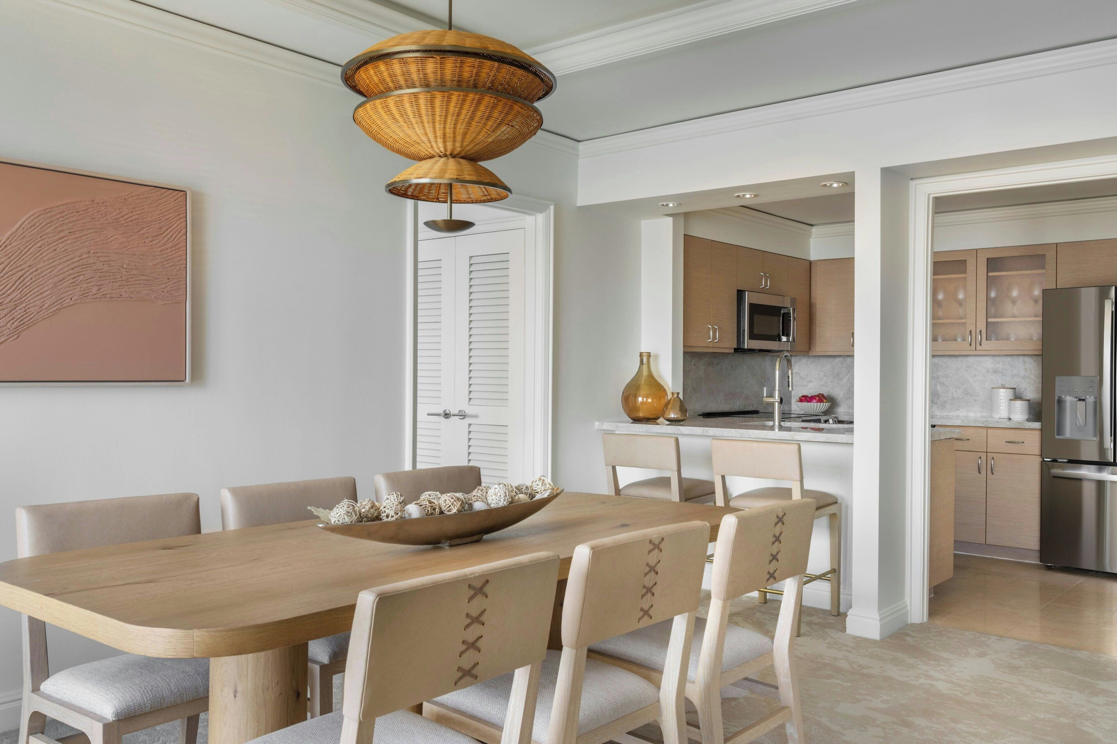 A modern kitchen with a wooden dining table and chairs, a hanging light fixture, and a view into the adjacent dining area.