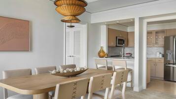 A modern kitchen with a wooden dining table and chairs, a hanging light fixture, and a view into the adjacent dining area.