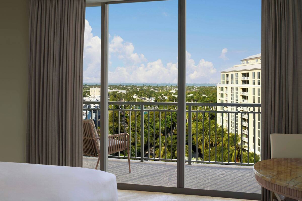 A hotel room with a large balcony, a bed, a chair, and a table.