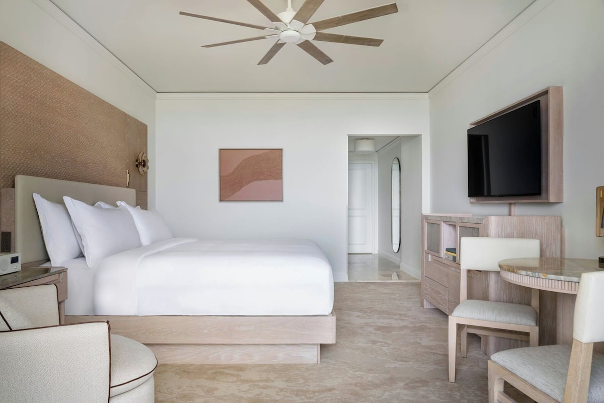 A modern hotel room with a large bed, a flat-screen TV, a desk with a chair, and a ceiling fan.