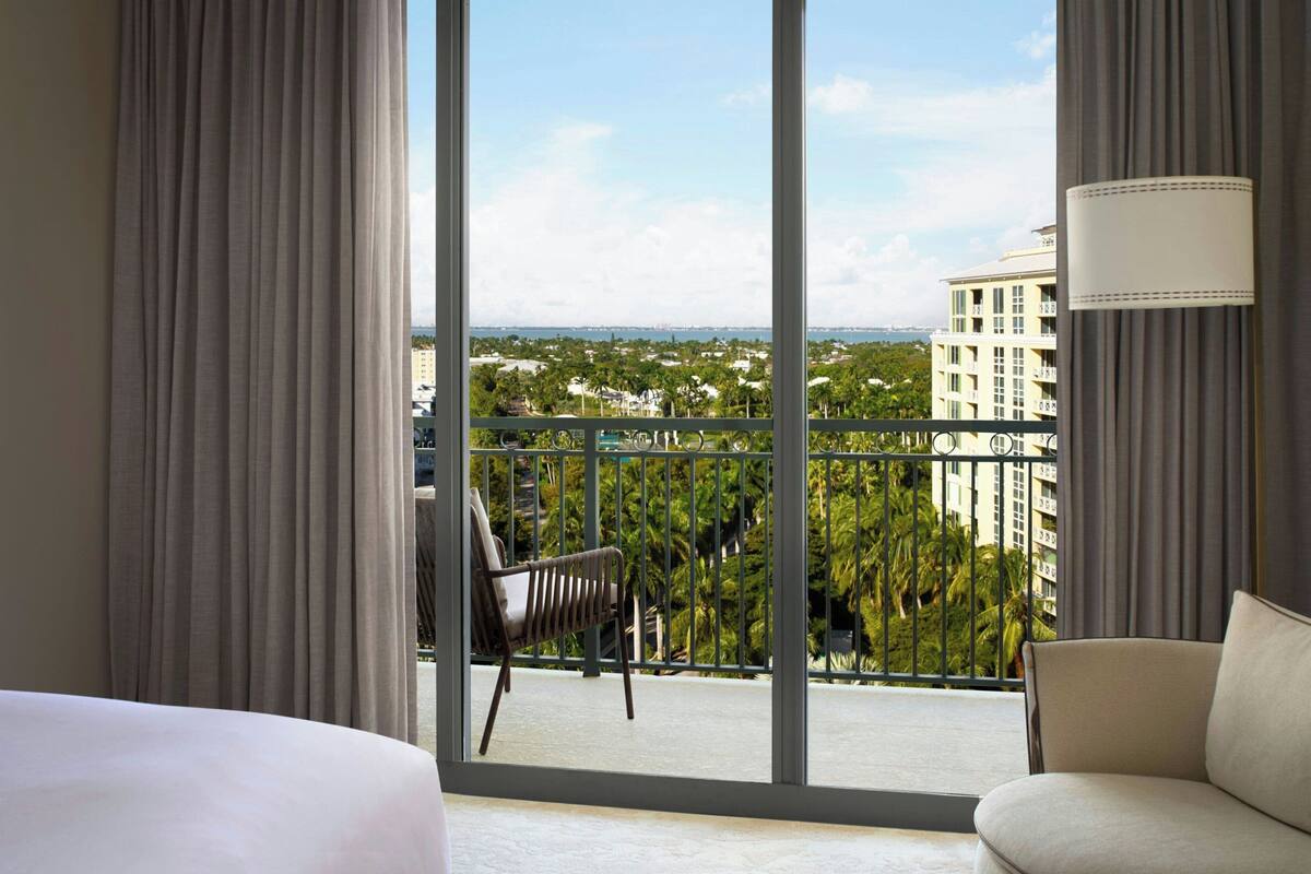 A hotel room with a balcony, a chair, and a view of a cityscape.