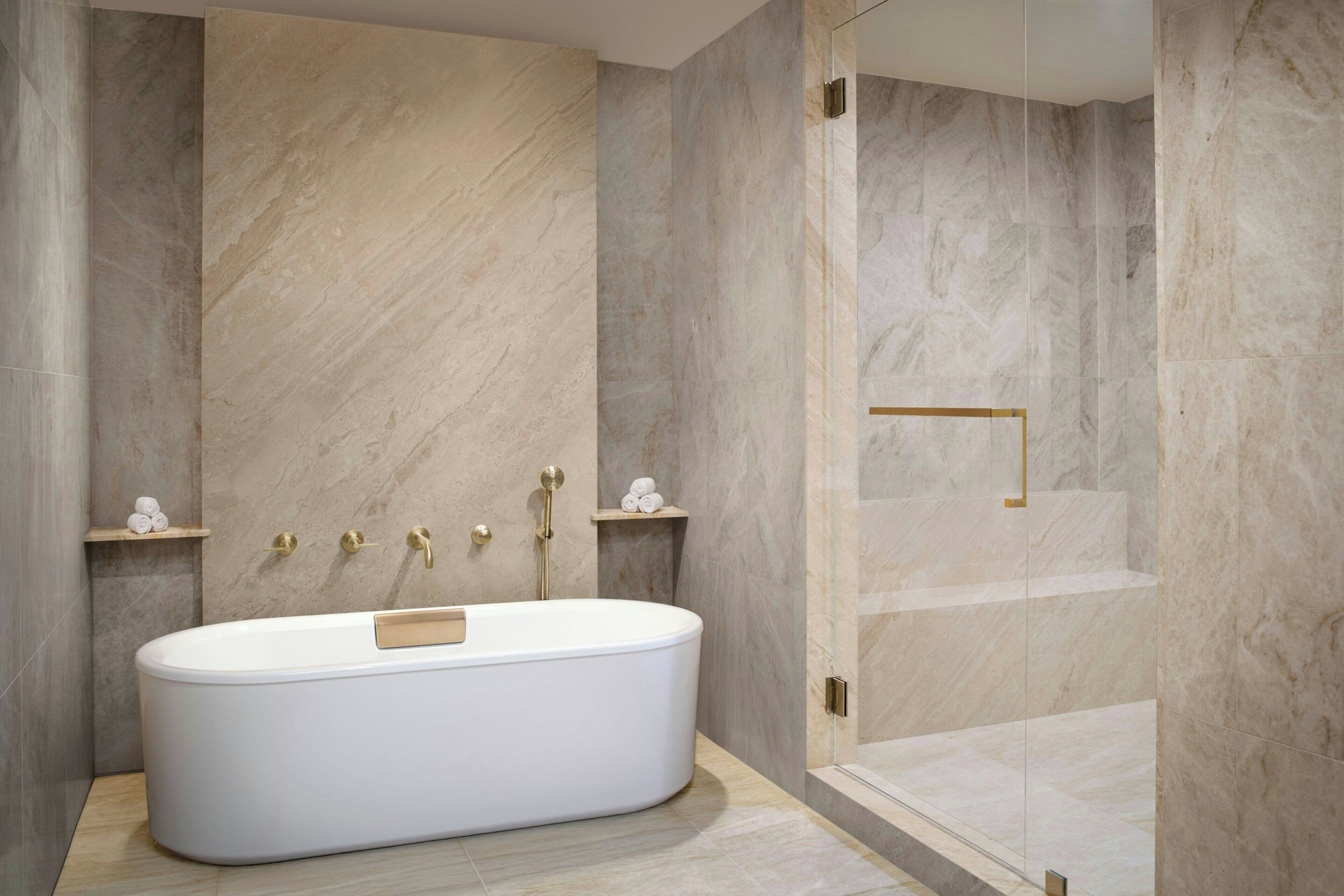 Un baño moderno con una bañera independiente, paredes de mármol y cabina de ducha con mampara de cristal.