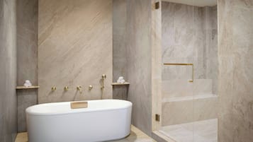 Un baño moderno con una bañera independiente, paredes de mármol y cabina de ducha con mampara de cristal.