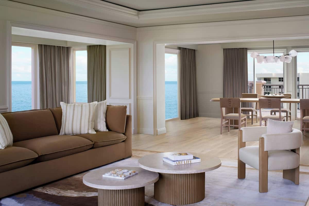 A modern living room with a brown sofa, round coffee tables, and a view of the sea through large windows.