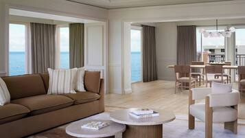 Een moderne woonkamer met een bruine bank, ronde salontafels en uitzicht op zee door grote ramen.
