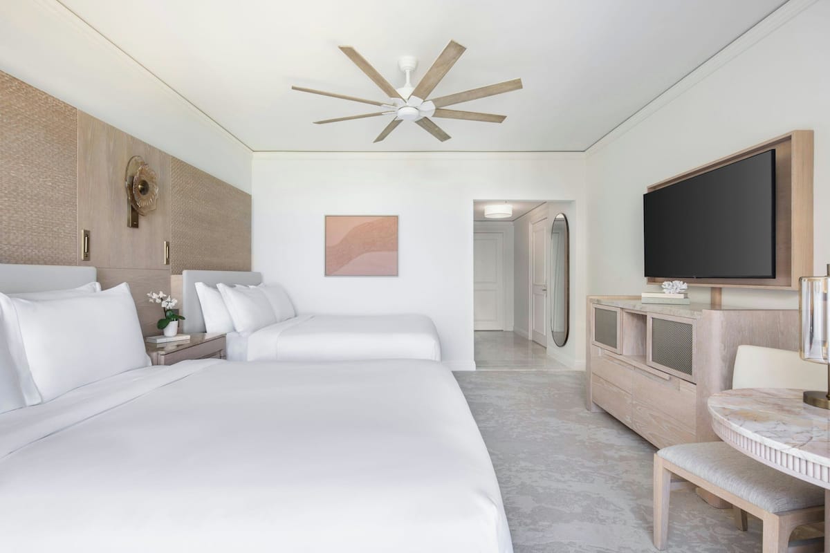 A hotel room with a large bed, a TV, a desk, and a ceiling fan.