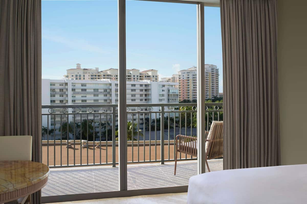 A hotel room with a large balcony, a bed, a chair, and a table.