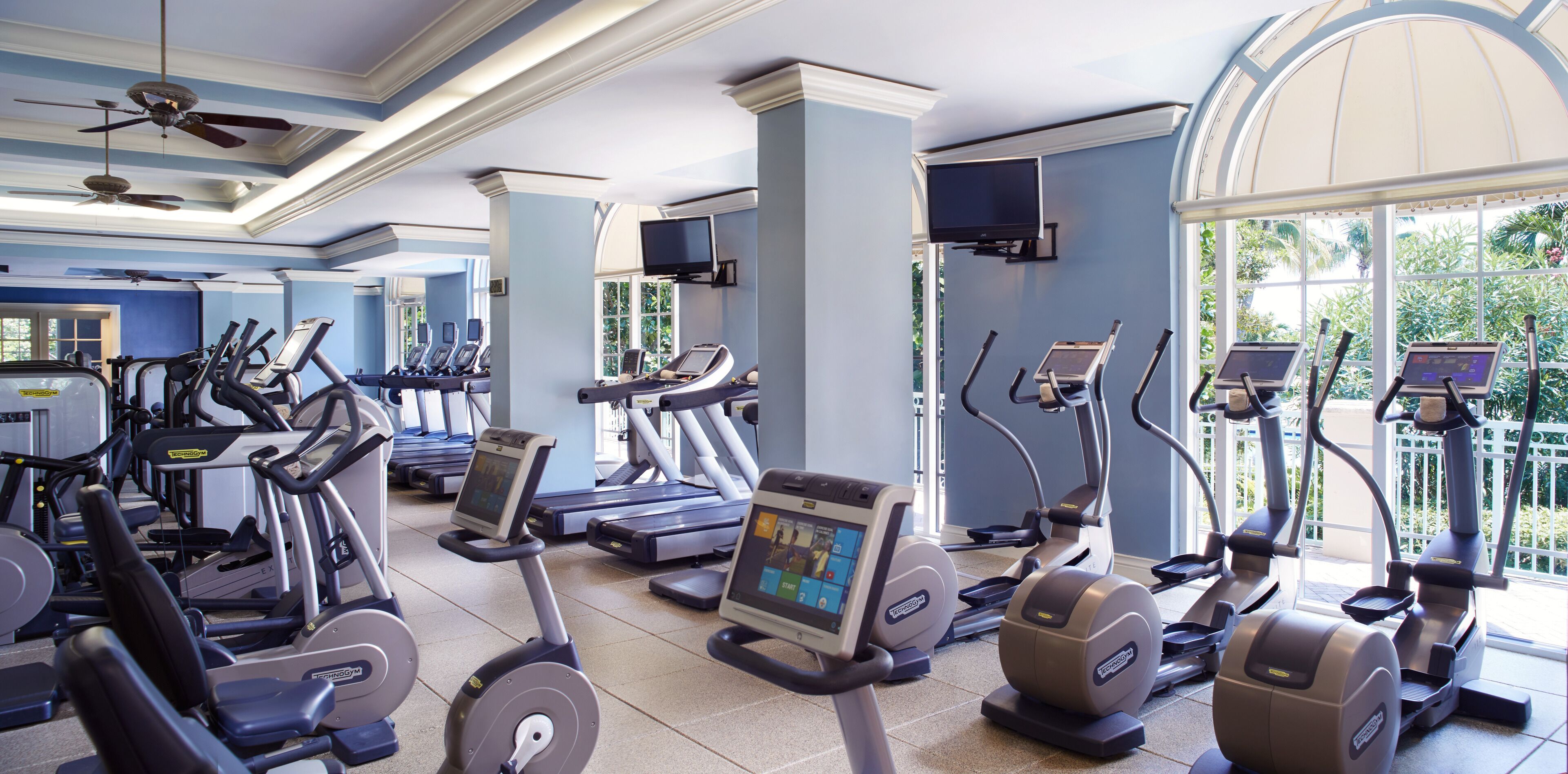 Un gimnasio con cintas de correr, elípticas y bicicletas estáticas, con amplias ventanas y un diseño moderno.