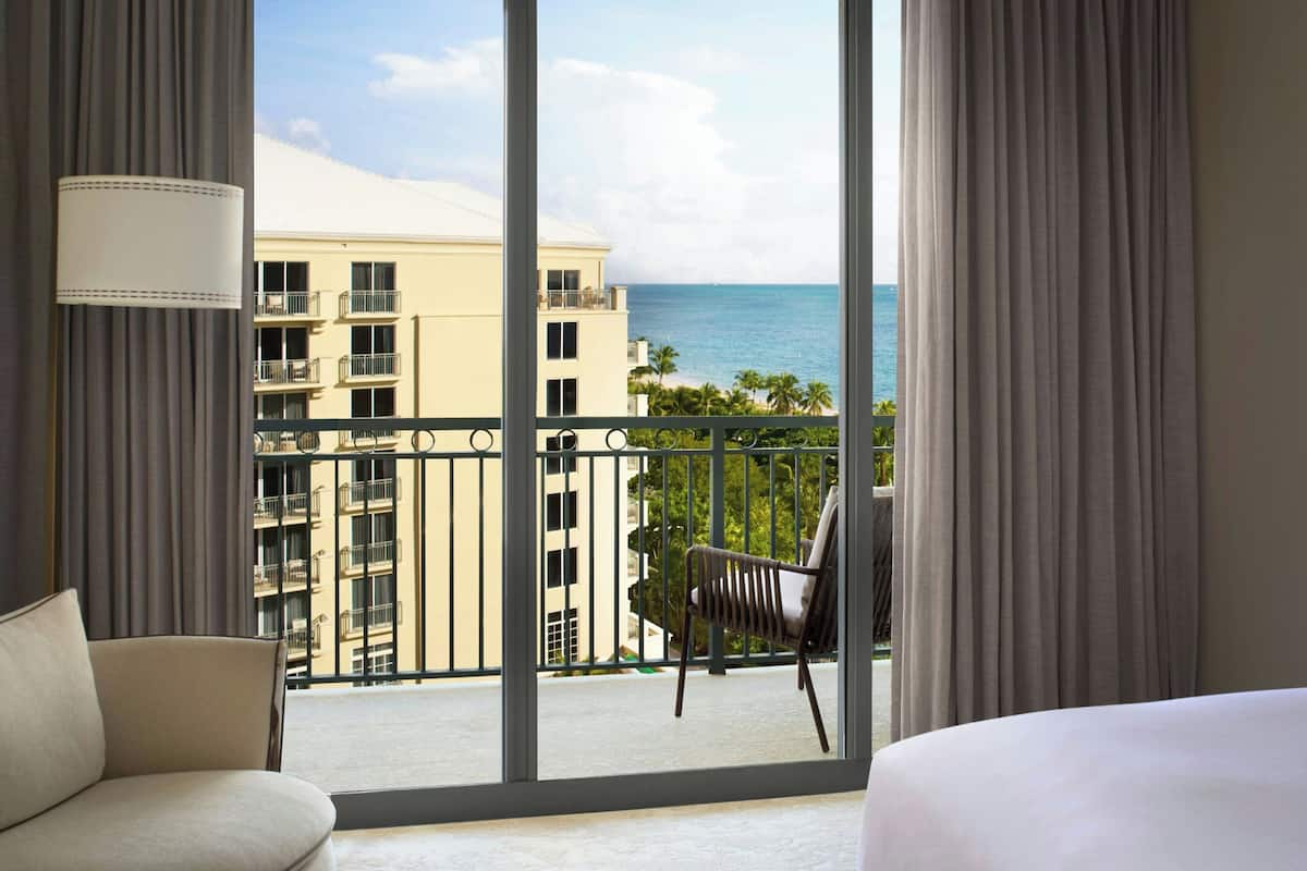 A hotel room with a large window offering a view of the ocean and a building across the street.