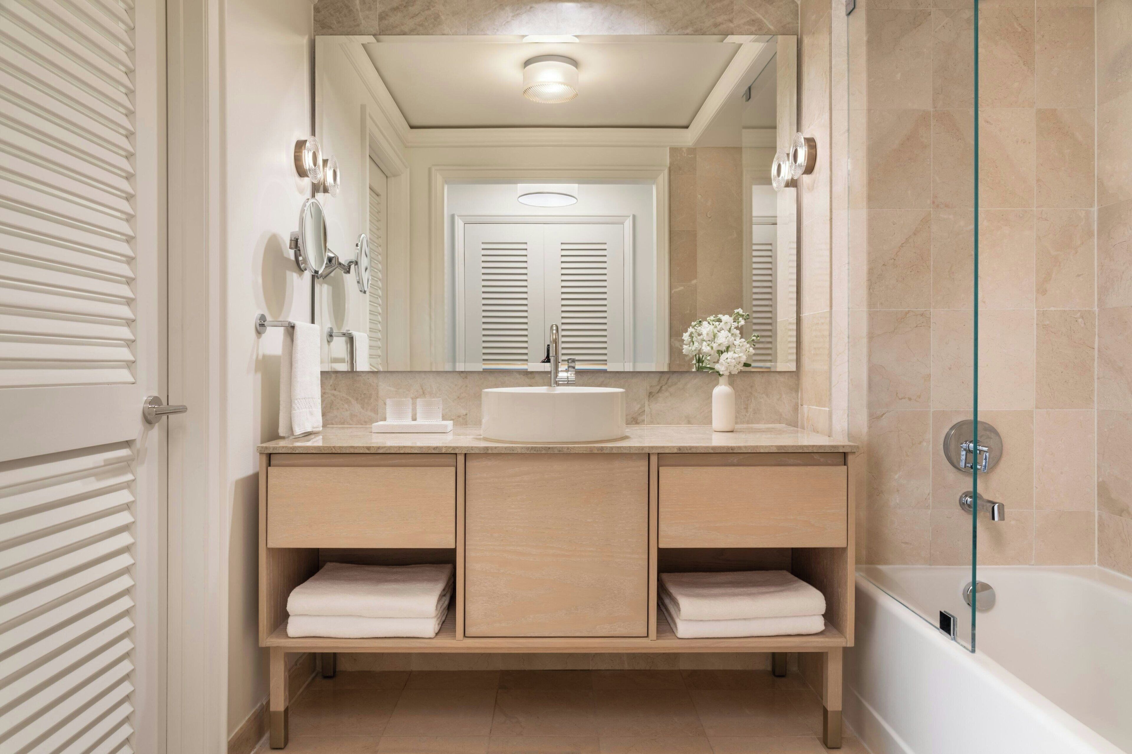 A modern bathroom with a large mirror, a sink, and a bathtub.