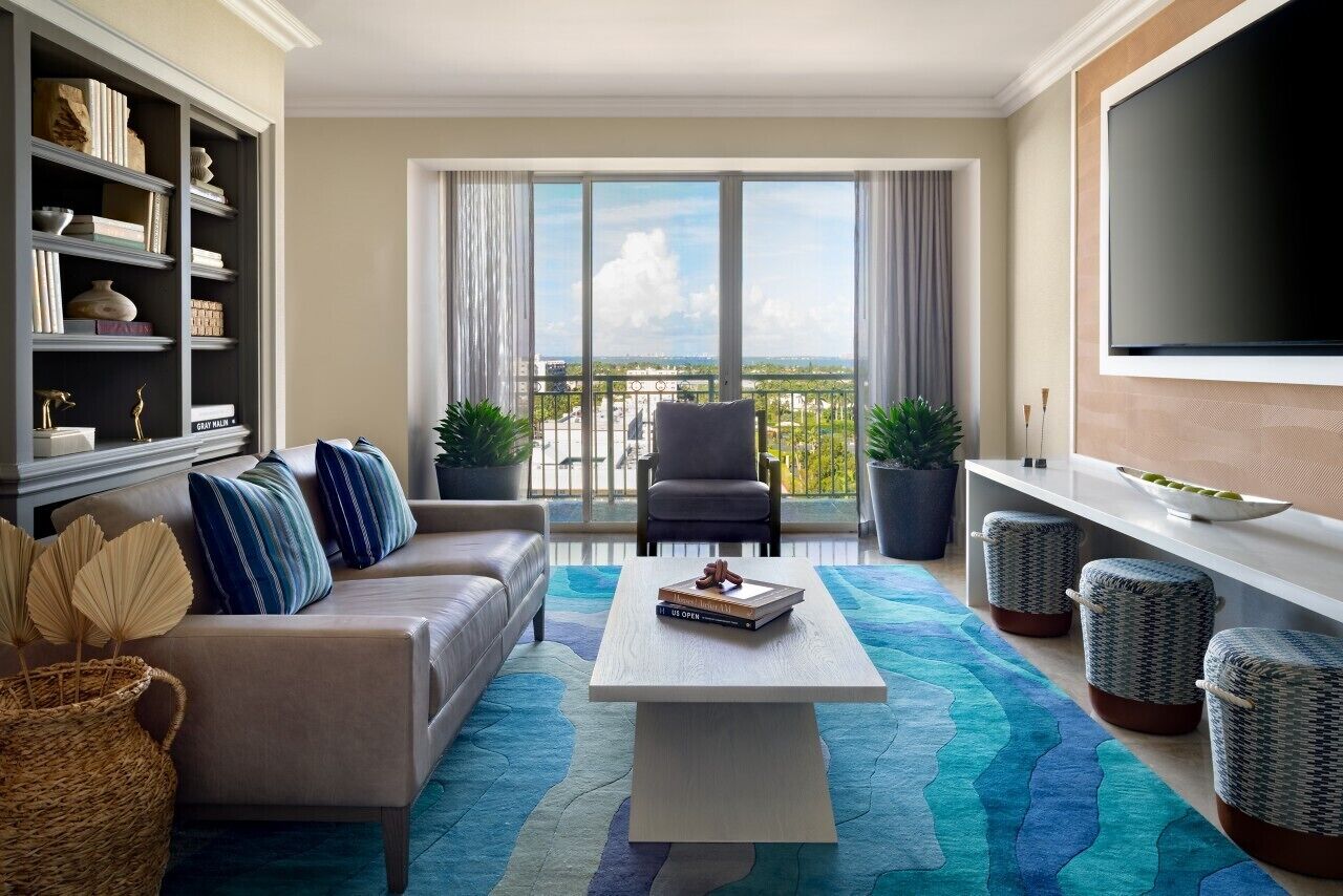 A modern living room with a sofa, coffee table, and a bookshelf. There is a balcony with a view of the city.