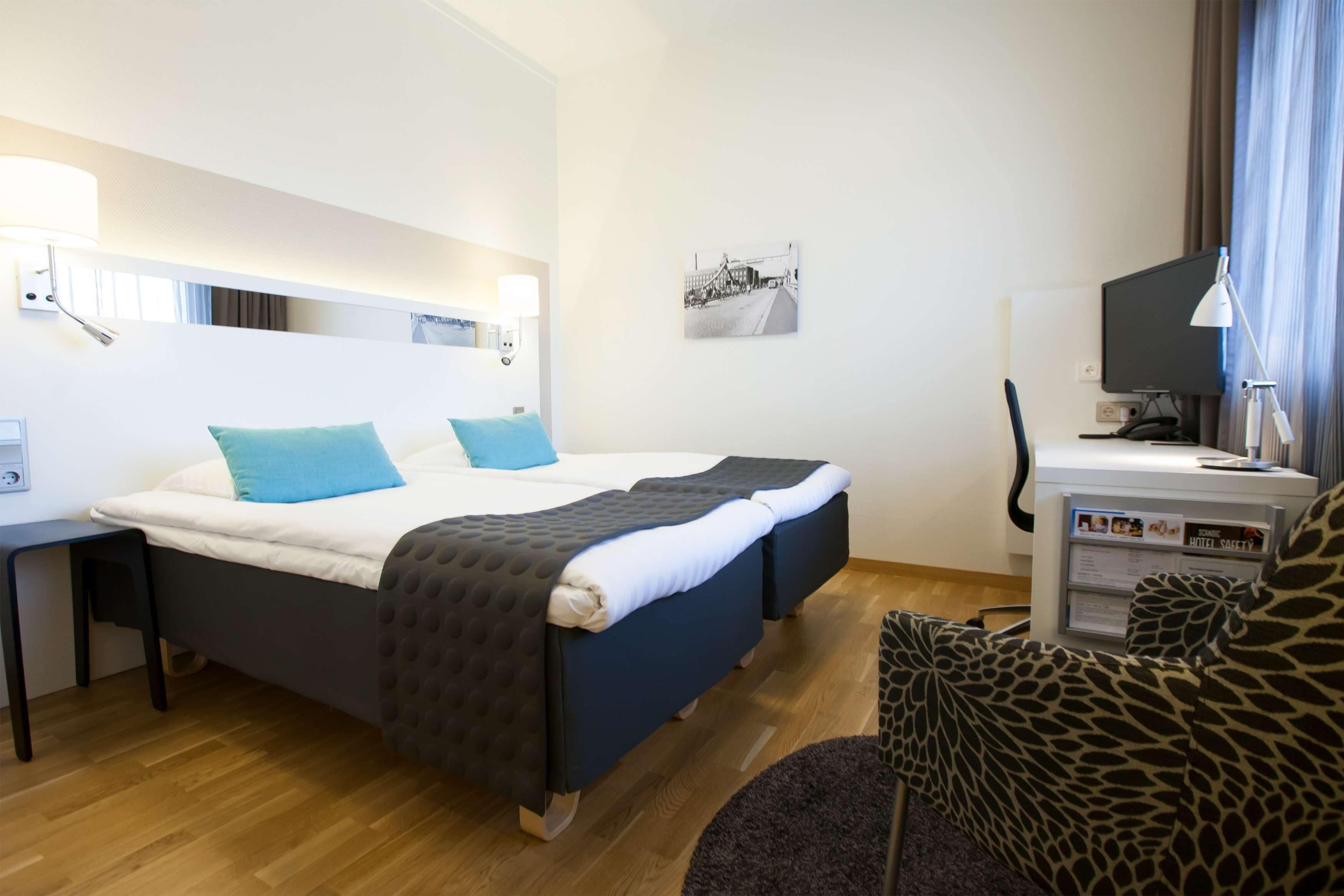 A hotel room with a bed, a desk, a chair, and a television.