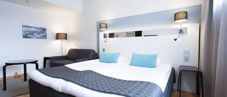 A modern hotel room with a large bed, two bedside lamps, a small table, and a chair.