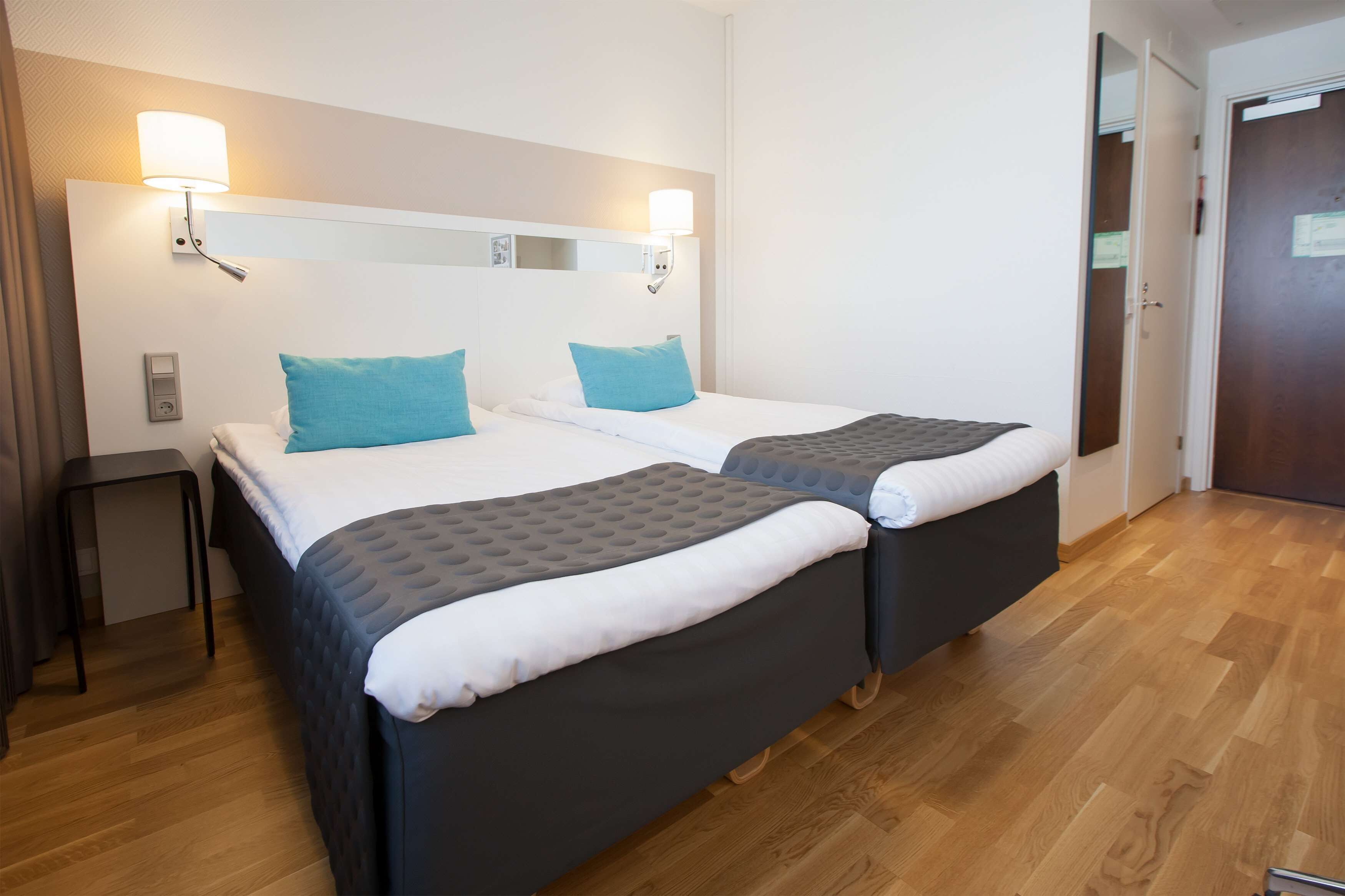 Une chambre d’hôtel avec deux lits, chacun doté d’une tête de lit, d’une table de chevet et d’une lampe fixée au mur.