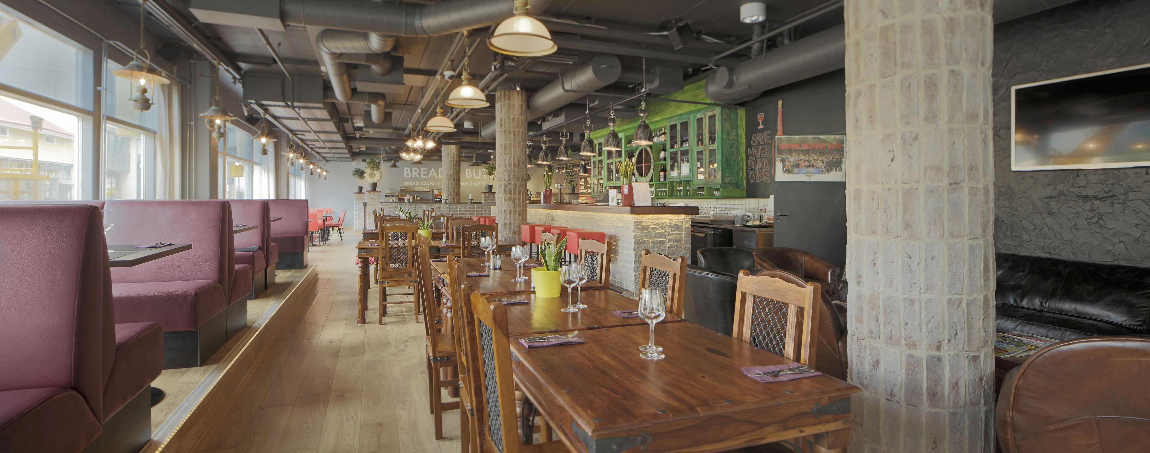 L'intérieur d'un restaurant avec des banquettes, des tables en bois et des lampes suspendues.