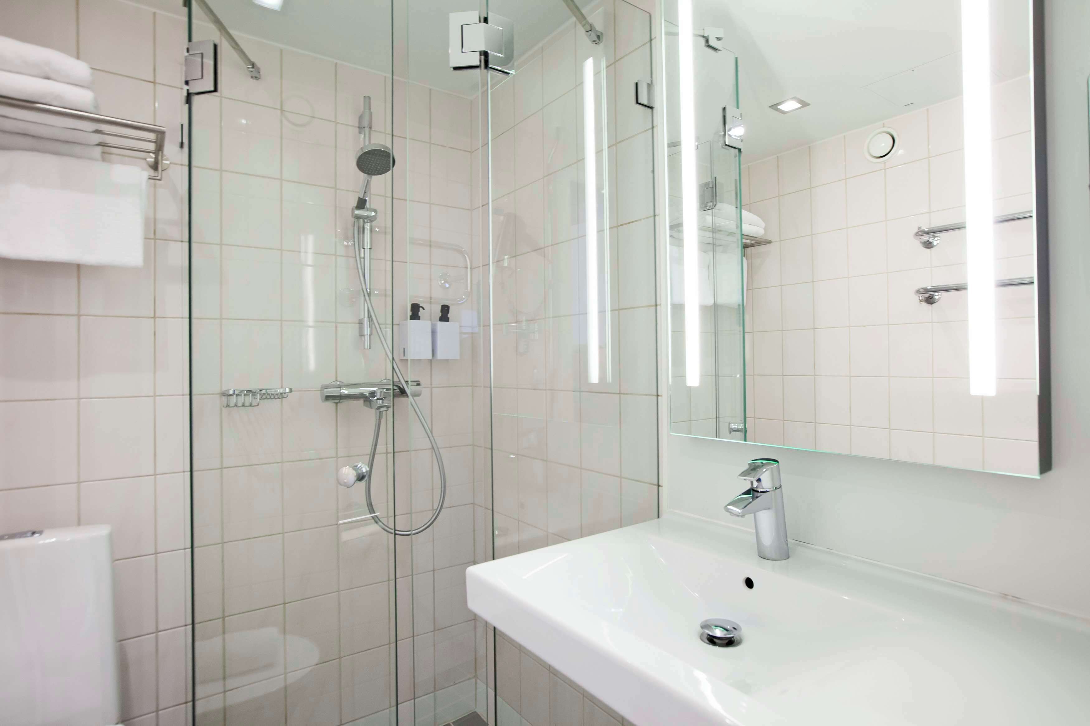 A modern bathroom with a glass-enclosed shower, a white sink, and a large mirror.