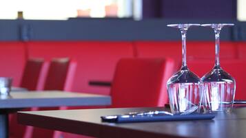 Une salle de restaurant avec deux verres à vin vides sur une table, des sièges rouges et une fenêtre en arrière-plan.